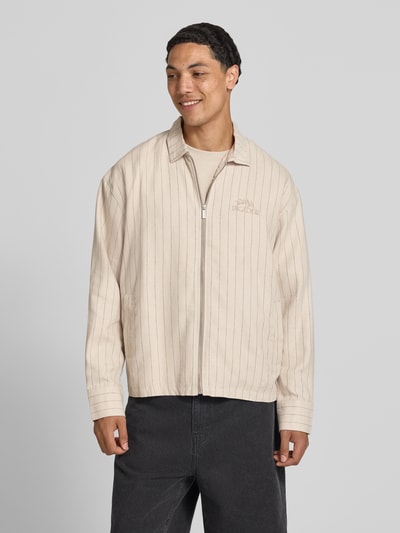 Männermodel trägt overshirt aus viscosemix mit logo-stitching model 'Sistelo' van Pegador in beige met strepen, relaxed fit, kentkraag, ritssluiting, ruglengte maat M 69 cm, ganzkörperansicht von vorne.