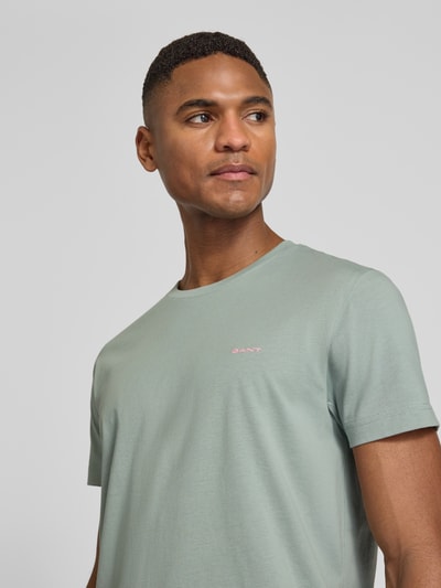 Mężczyznamodel nosi T-Shirt mit Label-Detail von Gant w kolorze miętowym, czysta bawełna, krój regular fit, dekolt okrągły, długość tyłu w rozmiarze M: 70 cm, zbliżenie górnej części ciała.