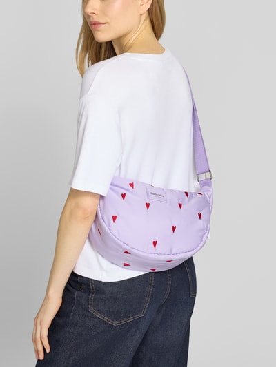 Frauenmodel trägt Handtasche mit Stitchings Modell 'Puffy Adult Fanny Pack' von STUDIO NOOS, fliederfarben mit roten Herzmustern, Schulterriemen, Hauptfach mit Reißverschluss, Ganzkörperansicht Rückansicht.