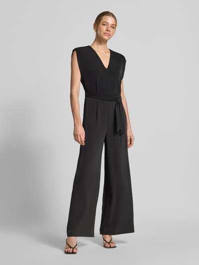 Frauenmodel trägt Jumpsuit mit V-Ausschnitt und Bindegürtel von Comma aus schwarzem Material-Mix mit Stretch-Anteil, Regular-Fit, Ganzkörperansicht von vorne. Rückenlänge 141 cm, Brustweite 36 cm, Gesamtlänge 144 cm, Innenbeinlänge 80 cm.