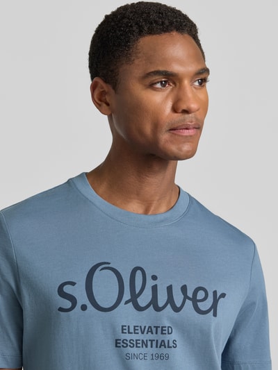 Mężczyzna nosi Regular Fit T-Shirt aus reiner Baumwolle von s.Oliver RED LABEL w kolorze niebieskim, gładki jersey, nadruk z logo, okrągły dekolt, krótki rękaw, uniszczegółowa faktura, nahaufnahme górnej części ciała.