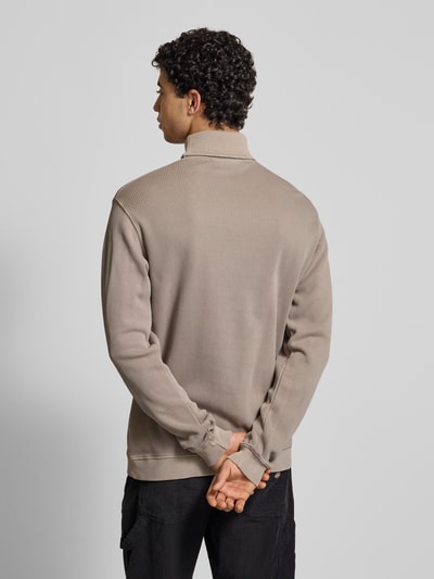 Męski model nosi Sweter z golfem w efekcie prążkowania z wyhaftowanym logo od Pegador, bawełna, krój relaxed fit, długość tyłu 70 cm, długość rękawów 70 cm, beżowy, faktura prążkowana, widok całej sylwetki z tyłu.
