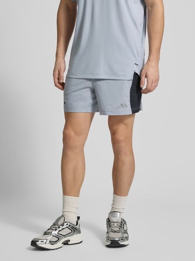 Männermodel trägt Regular Fit Sport-Shorts aus schnelltrocknendem Material von adidas Training, Mehrfarbig, Schriftzug-Print, seitliche Eingrifftaschen, perforierte Einsätze, reflektierender Logo-Print, elastischer Bundabschluss, Funktion: Schnelltrocknend, Feuchtigkeitsregulierend, Ganzkörperansicht von vorne.