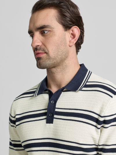 Männermodel trägt Slim Fit Poloshirt in Strick-Optik von MCNEAL mit Polokragen, creme mit dunkelblauen Streifen, Nahaufnahme Oberkörper.