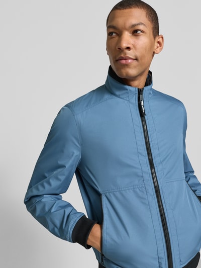 Männermodel trägt Regular Fit Jacke mit Stehkragen von MCNEAL in Blau mit Reißverschluss, Eingrifftaschen und elastischen Abschlüssen, Nahaufnahme Oberkörper. Rückenlänge 64 cm, Schulterbreite 43 cm, Brustweite 55 cm, Ärmellänge 67 cm.