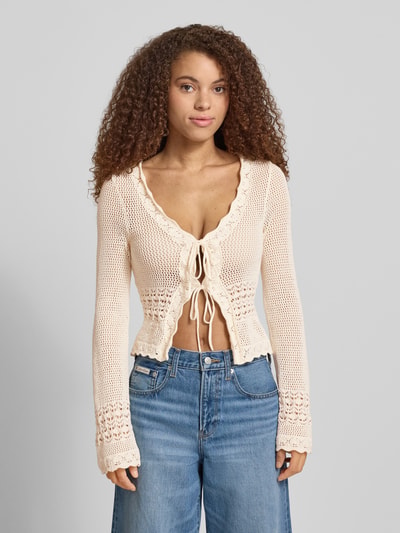 Frauenmodel trägt Strickjacke mit Schnürung von REVIEW in Creme, Baumwolle, Wellensaum, Regular Fit, kombiniert mit Jeans, Nahaufnahme Oberkörper.