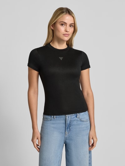 Vrouwenmodel draagt T-shirt uit viscosemix model 'LICIA' van GUESS, zwart, smalle fit, siersteentjes-logo, ronde hals, bovenlichaam close-up, context: dames trui, ruglengte maat S 52 cm.
