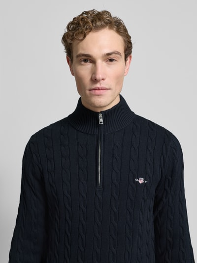 Männermodel trägt Strickpullover mit gerippten Abschlüssen von Gant, Reine Baumwolle, Slim-Fit, Stehkragen, kurzer Reißverschluss, Label-Stitching, Nahaufnahme Oberkörper.