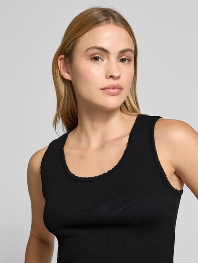 Kobiece model prezentuje top z okrągłym dekoltem model 'FARIDA' od Drykorn, czarna bawełna, drobne prążkowanie, dopasowany krój, długość tyłu w rozmiarze S 48 cm, zbliżenie na górną część ciała.