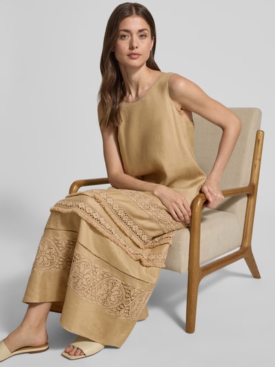 Kobieta nosi Fließendes Freizeitkleid aus reinem Leinen Modell 'DOLMEN' od Weekend Max Mara, beżowy, luźny, maxi, wzór allover, okrągły dekolt, aplikacja z koronki i etykieta, boczne kieszenie, materiał: czysty len, widok na górną część ciała z przodu.