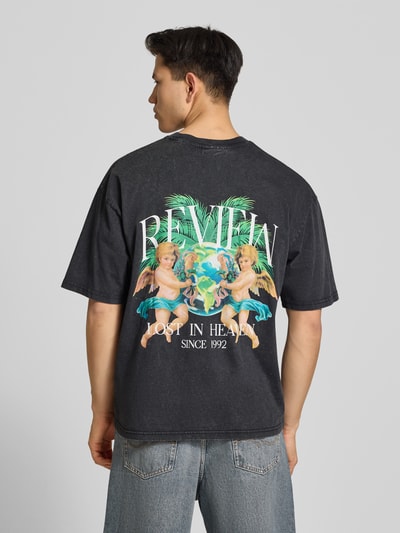 Männermodel trägt T-Shirt mit überschnittenen Schultern von REVIEW in Schwarz mit buntem Label-Print und Rundhalsausschnitt, Rückenansicht.