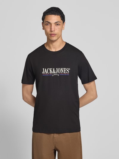 Męski model nosi t-shirt z nadrukiem z logo, czarny, prosty krój, bawełna, Model 'FREDERIKSBERG' od JACK & JONES, okrągły dekolt, długość tyłu w rozmiarze M: 70 cm, widok całej sylwetki z przodu