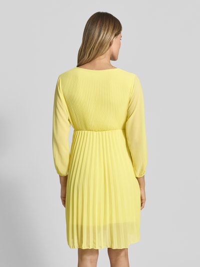 Frauenmodel trägt knielanges Kleid mit Plisseefalten Modell 'Im44sa' von ZABAIONE in Gelb, taillierter Schnitt, Rückenlänge 90 cm, Ganzkörperansicht Rückansicht.