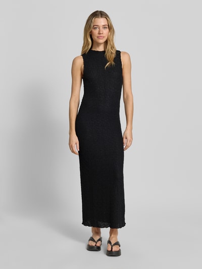 Modelka kobieca ma na sobie czarne Maxikleid mit Rundhalsausschnitt Modell 'FALL' od Vila z materiału ze stretchem, krój prosty, Ganzkörperansicht von vorne, długość tyłu w rozmiarze S: 136 cm, szerokość w rozmiarze S: 33 cm.
