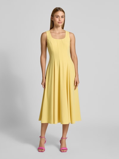 Frauenmodel trägt Midikleid mit Rundhalsausschnitt Modell 'ARLOTT' von Ted Baker in Gelb, A-Linie, breite Träger, Ganzkörperansicht von vorne.