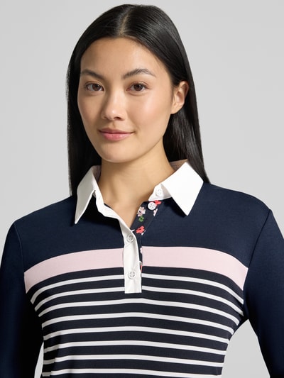 Kobieta modelka nosi Slim Fit Poloshirt aus Baumwoll-Mix od Marc Cain, ciemnogranatowy, jasnoróżowe i białe paski, kołnierzyk polo, mieszanka bawełny, krój slim fit, długość tyłu w rozmiarze 36: 56 cm, bluzka z długim rękawem, zbliżenie górnej części ciała.