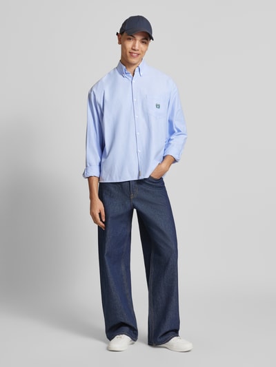 Męski model nosi Regular Fit Freizeithemd mit Motiv-Stitching od ANOTHER COTTON LAB, bawełniany miks, krój regular fit, model 'Everyday Pocket', kołnierzyk button-down, zapięcie na guziki, kieszeń na piersi, dekoracyjne przeszycia, detal z logo, sportowe mankiety, długość tyłu w rozmiarze M: 71 cm, szerokość ramion w rozmiarze M: 53 cm, długość rękawa w rozmiarze M: 62 cm, błękitna tkanina, ciemnoniebieskie spodnie, białe buty, pełny widok z przodu.