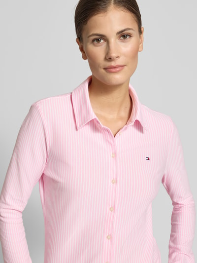 Vrouwenmodel draagt Slim Fit Hemdbluse uit katoenmix van Tommy Hilfiger met all-over streepmotief, gestikt logo, knoopsluiting, lange mouw, overhemdkraag, mouwboord. Nahaufnahme bovenlichaam.