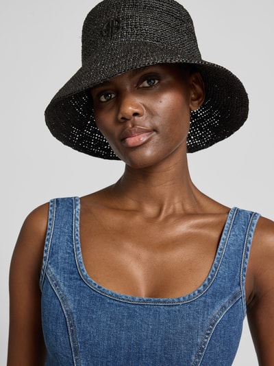 Frauenmodel trägt Bucket Hat in Flecht-Optik von Anine Bing aus reiner Baumwolle mit Logo-Detail, runder Optik, breite Krempe, Nahaufnahme Oberkörper.