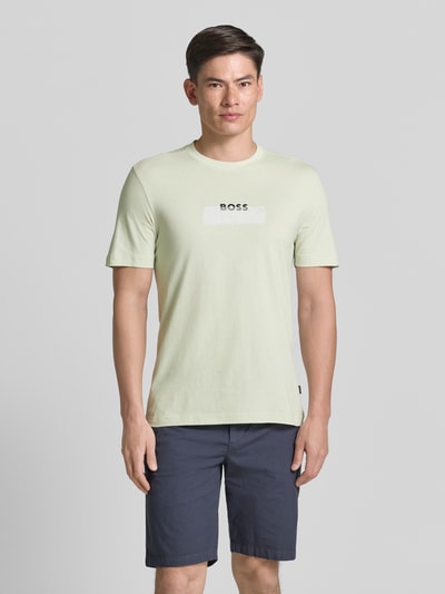 Mężczyzna nosi Regular Fit T-Shirt aus reiner Baumwolle Modell 'Te_LOGOTAPE' von BOSS Orange, jasny materiał, nadruk logo, krój regular fit, unikalna faktura jersey, widok całej sylwetki z przodu.