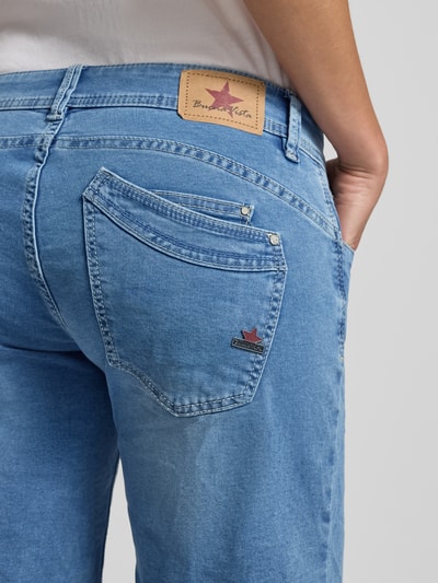 Frauenmodel trägt Jeansshorts mit asymmetrischem Knopfverschluss Modell 'Malibu' von Buena Vista aus Baumwoll-Mix mit Stretch-Anteil, 5-Pocket-Design, helle Waschung, Detailaufnahme Rückansicht.