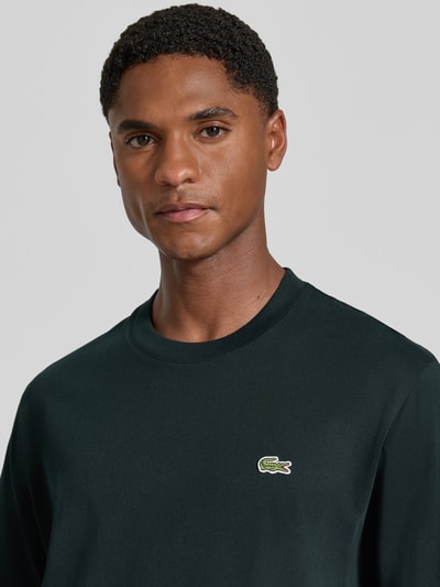 Männermodel trägt Regular Fit T-Shirt aus reiner Baumwolle von Lacoste, dunkle Farbe mit glatter Textur, Nahaufnahme Oberkörper. Herren T-Shirt von Lacoste