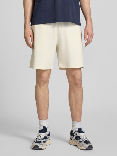 Männermodel trägt Shorts mit elastischem Bund und Label-Stitching von CHAMPION in Creme, aus Baumwoll-Mix, Ganzkörperansicht von vorne.