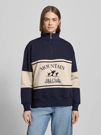 Frauenmodel trägt Sweatshirt mit Reißverschluss Modell 'Cosette' von LeGer by Lena Gercke in Dunkelblau und Beige, Baumwoll-Mix, Relaxed Fit, Stehkragen, Stitching, Ganzkörperansicht von vorne.