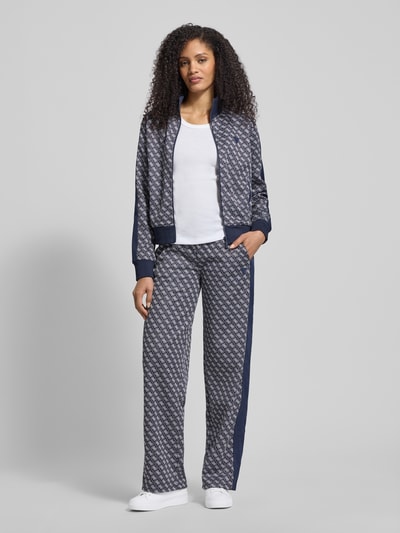 Frauenmodel trägt Wide Leg Sweatpants im Allover-Look Modell 'MAYA' von Guess Activewear mit elastischem Bund, Ganzkörperansicht von vorne.