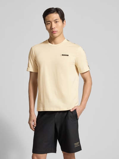 Männermodel trägt Regular Fit T-Shirt mit Logo-Patch von EA7 Emporio Armani in Beige, reine Baumwolle, Rundhalsausschnitt, Ganzkörperansicht von vorne.