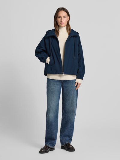 Frauenmodel trägt Relaxed Fit Regenjacke mit Baumwoll-Anteil Modell 'ROMANA' von Weekend Max Mara in Dunkelblau, mit Kapuze, langarm, unifarben, seitliche Eingrifftaschen, Logo-Patch, wasserabweisend, Ganzkörperansicht von vorne.
