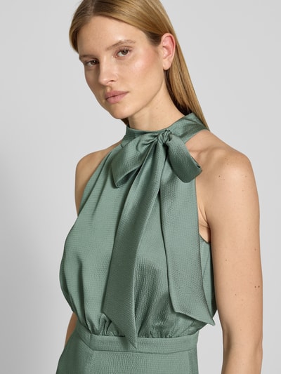 Frauenmodel trägt Jumpsuit mit Schleifen-Detail von SWING in zartem Grün, leicht glänzende Struktur, Regular Fit, Neckholder, Nahaufnahme Oberkörper, Rückenlänge bei Größe 36: 40 cm, Brustweite bei Größe 36: 36 cm, Gesamtlänge bei Größe 36: 152 cm, Innenbeinlänge bei Größe 36: 83 cm, rückseitiger Reißverschluss.