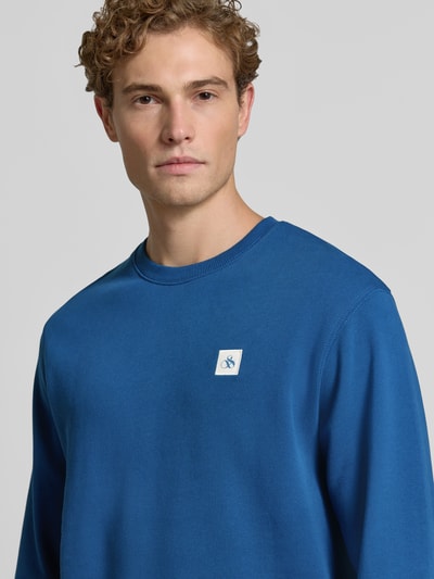 Männermodel trägt blauw sweatshirt met labelbadge en ronde hals, puur katoen, regular fit van Scotch & Soda, nahaufnahme bovenlichaam.