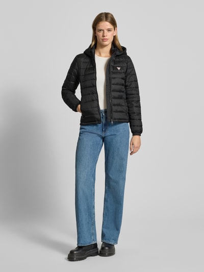 Vrouwenmodel draagt Gewatteerd jack met capuchon van Guess Jeans, regular fit, ritssluiting, labeldetail, ritszakken, zwart; volledige vooraanzicht.