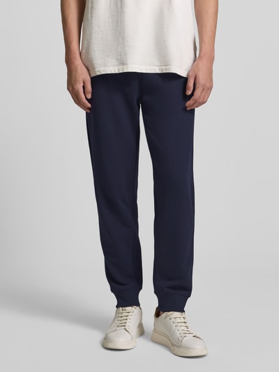 Männermodel trägt Sweatpants mit elastischem Bund van Gant, katoenmix, los model, steekzakken, achterzak, donkerblauw, binnenbeenlengte maat M 73 cm, detailaufnahme onderlichaam