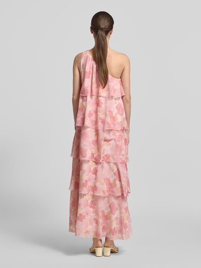 Vrouwenmodel draagt uitlopend maxi-jurk met all-over bloemenmotief, ruchedetail en one-shoulder look, model 'FELICIA' van Vero Moda in chiffon, maxi lengte, rugdecolleté, volantzoom, roze tinten, materiaalverwerking: chiffon. Ganzkörperansicht Rückansicht.