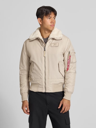 Männermodel trägt Bomberjacke mit Label-Patch und Kentkragen von Alpha Industries, beige Farbe, Teddyfellkragen, Ganzkörperansicht von vorne. Regular Fit, Reißverschluss, Reißverschlusstasche am Ärmel mit Label-Patch, Eingrifftaschen, gerippte Abschlüsse.