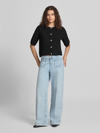 Frauenmodel trägt Boxy Fit Strickjacke aus Rippstrick Modell 'SILLY' von PIECES in Schwarz, Knopfleiste, Melange-Optik, Ganzkörperansicht von vorne.