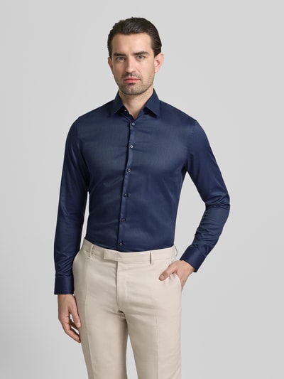 Männermodel trägt Slim Fit Businesshemd in Premiumqualität von Jake*s, dunkelblaues Allover-Muster, Kentkragen, Baumwolle, Ganzkörperansicht von vorne.