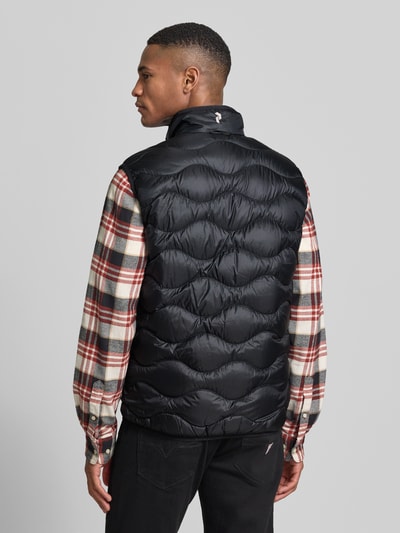 Männermodel trägt Regular Fit Weste aus reinem Alcantara Modell 'Helium' von Peak Performance in Stepp-Optik mit Logo-Stitching, Ganzkörperansicht Rückansicht. Rückenlänge bei Größe M: 67 cm, Schulterbreite bei Größe M: 39 cm, Brustweite bei Größe M: 47 cm, gefütterter Stehkragen, Reißverschluss, schwarze Farbe, glänzende, glatte Textur.