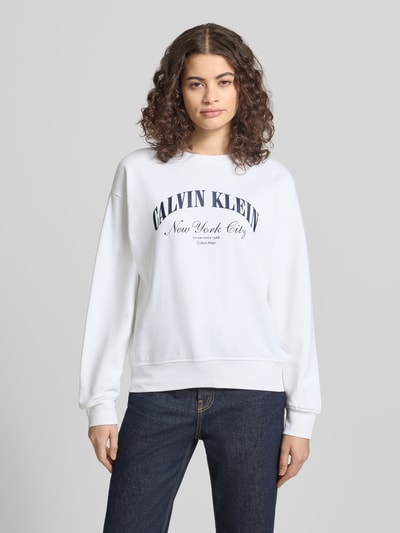 Kobiece model prezentuje bluzę Sweatshirt mit Label-Print Modell 'GRAPHIC' od Calvin Klein Jeans, mieszanka bawełny i elastanu, luźny krój, okrągły dekolt, nadruk z logo, elastyczne wykończenia, kolor biały, gładka faktura, widok całej sylwetki z przodu.