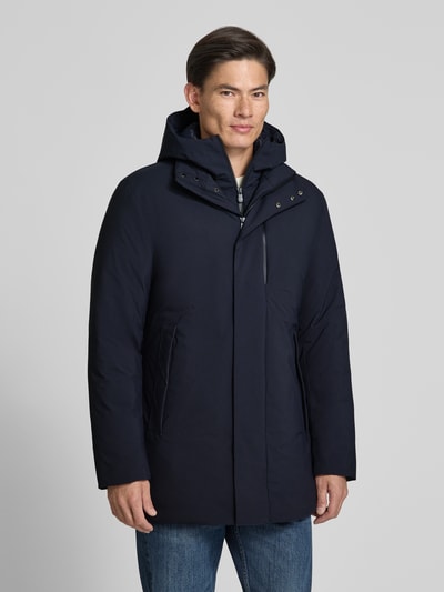 Męski model nosi granatowy Mantel mit Kapuze und Brusttasche Modell 'SESLE' od Save The Duck, prosty fason, tekstura gładka, widoczne boczne kieszenie i kaptur, jeansy, widok z przodu, zdjęcie całej sylwetki.