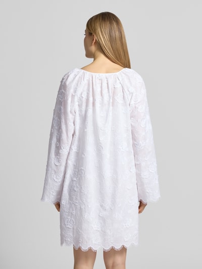 Frauenmodel trägt Minikleid mit Spitze und Kimonoärmeln von MICHAEL Michael Kors in Weiß, florale Textur, Rückenansicht Ganzkörperansicht. Reine Baumwolle, Loose Fit, blickdichtes Unterkleid, Serafino-Ausschnitt mit Schnürung.