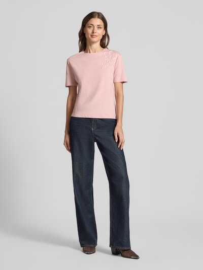 Frauenmodel trägt Regular Fit T-Shirt aus reiner Baumwolle mit Blumen-Applikation von Christian Berg Woman in Rosa, kurzärmlig, Ganzkörperansicht von vorne.