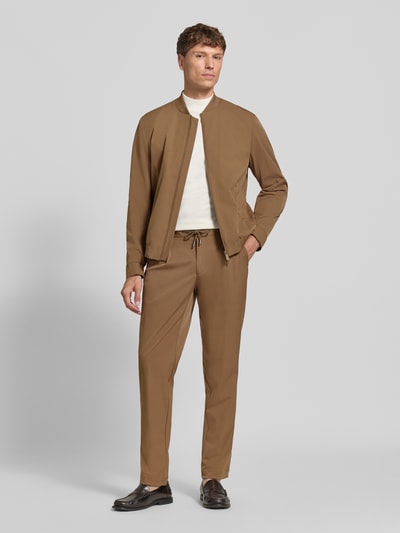 Męski model nosi Hose mit elastischem Bund und Tunnelzug od bugatti, materiał z domieszką stretchu, krój regular fit, tylne kieszenie, kolor brązowy, szerokość w rozmiarze 50: 44 cm, długość nogawki od wewnątrz w rozmiarze 50: 83 cm, widok całej sylwetki z przodu