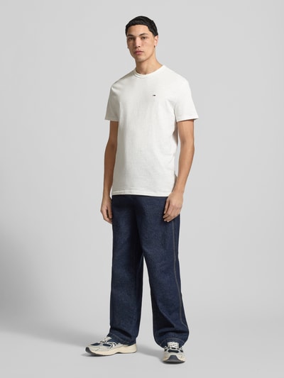 Männermodel trägt Regular Fit T-Shirt aus reiner Baumwolle von Tommy Jeans, unifarben, Logo-Detail, Kurzarm, Ganzkörperansicht von vorne.