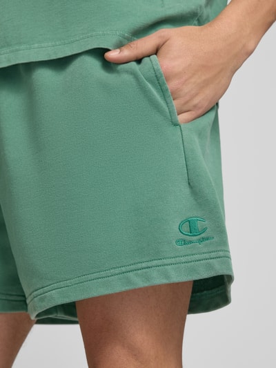 Männermodel trägt Sweatshorts mit Eingrifftaschen von CHAMPION in Grün, Baumwoll-Mix, Label-Stitching, Nahaufnahme Oberschenkel.