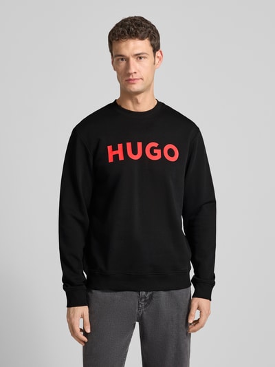 Męski model nosi czarne Sweatshirt mit Label-Detail Modell 'Dem' od HUGO z czerwonym logo, bawełna, luźny krój, widok z przodu, całej sylwetki.
