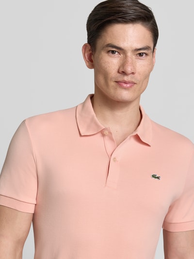 Männermodel trägt Regular Fit Poloshirt aus reiner Baumwolle von Lacoste in Optik: Unifarben mit Logo-Detail, Nahaufnahme Oberkörper.