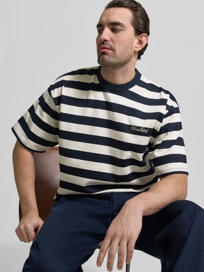 Männermodel trägt Relaxed Fit T-Shirt mit Logo-Stitching Modell 'Beam' von Woodbird aus reiner Baumwolle mit Rundhalsausschnitt, Nahaufnahme Oberkörper.